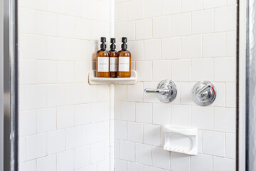 Minimalist shower interior with white tile walls and amber amenity bottles including shampoo body...