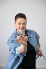 Smiling female hairstylist holding scissors, posing in modern barbershop. Professional hairdresser showing haircut tool, beauty salon service and hairstyling concept.
