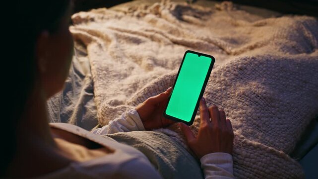 Woman scrolling greenscreen mobile phone relaxing comfortable home bed closeup.