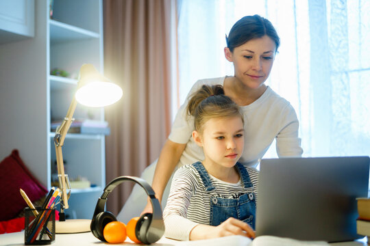 mother helping teen daughter studying computer while doing homework for school