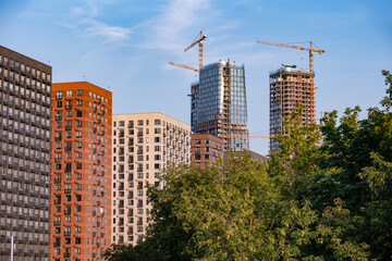 Fototapeta premium Urban cityscape with new residential towers rising above buildings, cranes on a blue sky