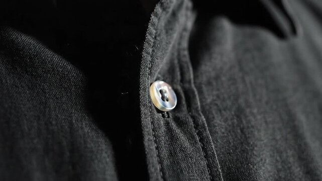 Close-up of a dark button-down shirt, buttoned, featuring detailed fabric texture under dramatic, moody lighting