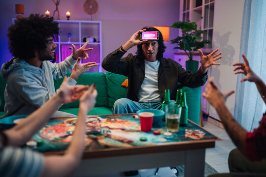 Friends playing charades game at home party, enjoying fun evening social gathering in living room