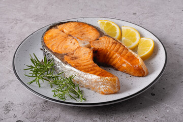 Seared salmon steak with rosemary and lemon pieces on grey table