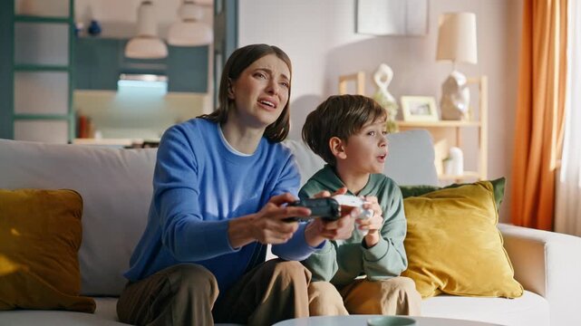 Sad mother losing video game sitting home couch with happy little son closeup. 