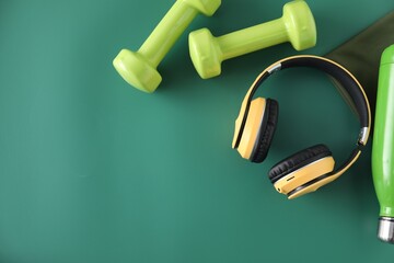 Yellow headphones and dumbbells on green background, flat lay. Space for text