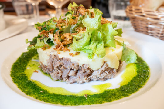French dish parmentier of candied duck, shredded canard confit with potatoes puree and green pesto, served in traditional bistro bouillon restaurant in Paris