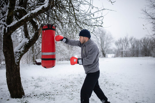 A man boxing in a winter snowy garden on a punching bag, a boxing class outdoors