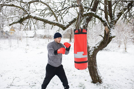A man boxing in a winter snowy garden on a punching bag, a boxing class outdoors