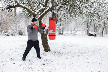 A man boxing in a winter snowy garden on a punching bag, a boxing class outdoors