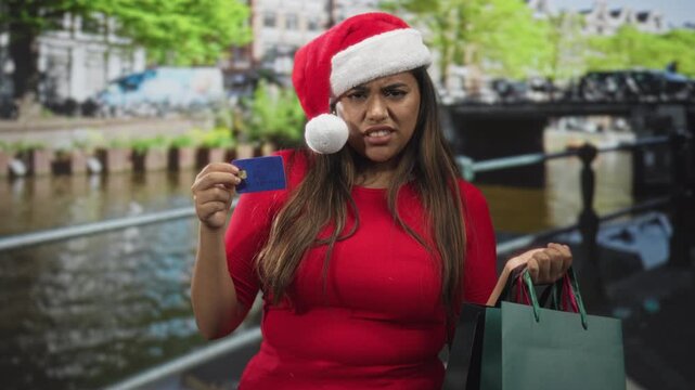 Plus size woman holding creditcard and shopping bags while grimacing on street; holiday frustration.