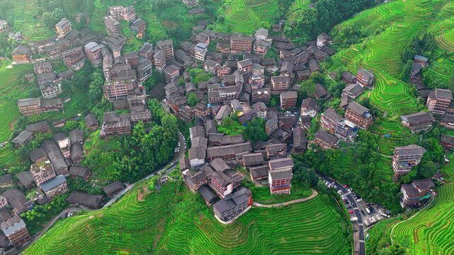 Aerial view of traditional wooden stilt houses and lush terraced fields in Guilin, China.
