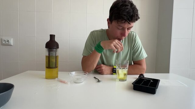 Man wearing green shirt calmly sipping homemade drink in kitchen setting