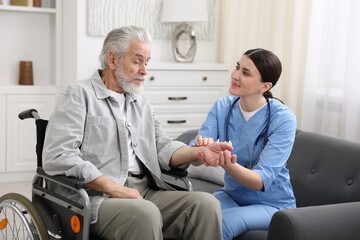 Obraz premium Care worker checking senior man's pulse in wheelchair indoors