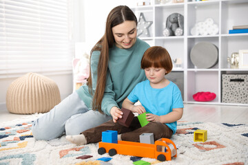 Naklejka premium Mother and her son playing with toys on floor at home