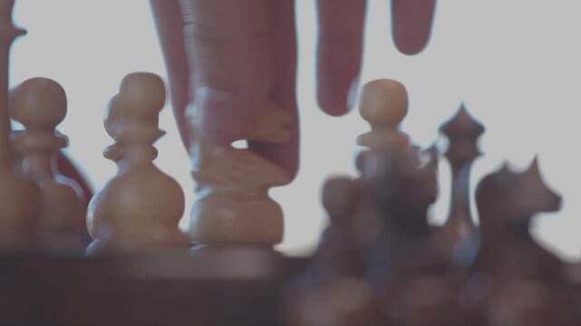 Two focused players are engaged in an intense game of chess. The camera captures a detailed close-up of a hand strategically moving a pawn across the wooden board.