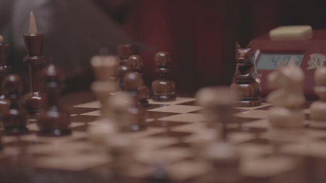 Two focused players are engaged in an intense game of chess. The camera captures a detailed close-up of a hand strategically moving a pawn across the wooden board.