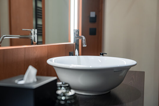 White vessel sink and tall chrome faucet on dark wood countertop, warm wood mirror with vertical lighting, black accents, bright even lighting in Dolomites