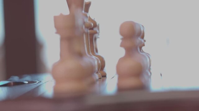 Two focused players are engaged in an intense game of chess. The camera captures a detailed close-up of a hand strategically moving a pawn across the wooden board.