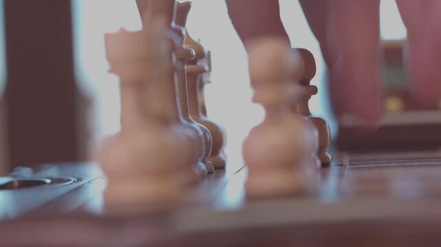 Two focused players are engaged in an intense game of chess. The camera captures a detailed close-up of a hand strategically moving a pawn across the wooden board.