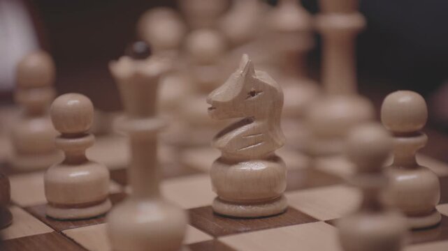 Two focused players are engaged in an intense game of chess. The camera captures a detailed close-up of a hand strategically moving a pawn across the wooden board.