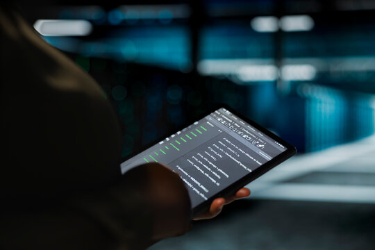 Data center computer scientist using tablet to optimize network infrastructure, planning capacity. Employee managing server room resources with device for improved reliability and uptime