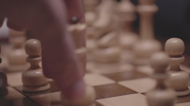 Two focused players are engaged in an intense game of chess. The camera captures a detailed close-up of a hand strategically moving a pawn across the wooden board.