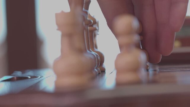 Two focused players are engaged in an intense game of chess. The camera captures a detailed close-up of a hand strategically moving a pawn across the wooden board.