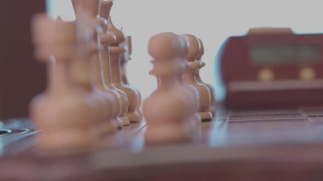 Two focused players are engaged in an intense game of chess. The camera captures a detailed close-up of a hand strategically moving a pawn across the wooden board.
