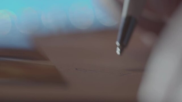 A captivating macro shot shows a ballpoint pen writing on paper in a spiral notebook. The shallow depth of field creates beautiful bokeh lights in the blurred background