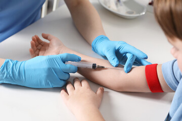 Nurse drawing little boy's blood sample in clinic, closeup