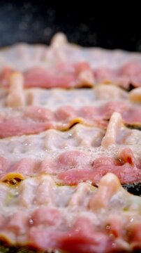 Sizzling raw bacon strips on skillet, prep cook prepping slices, pink fat bubbling, oil droplets shimmering, closeup texture evokes morning aroma