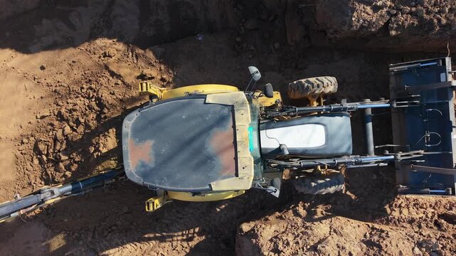 Excavator digging and lifting soil inside deep construction pit while performing foundation excavation at building site.