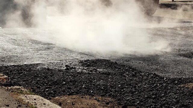 Road roller compacting freshly laid asphalt during street paving. Close view of heavy construction machinery working on new road surface.