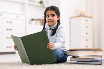 Fototapeta premium Cute little girl reading book on floor at home