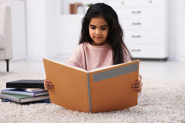 Fototapeta premium Cute little girl reading book on floor at home