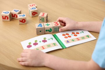 Little boy playing with cubes at wooden table, closeup. Educational toy