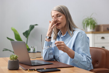 Senior woman feeling fatigue at wooden desk in office