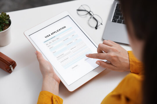 Visa application. Woman using tablet computer to fill in online form at table, closeup