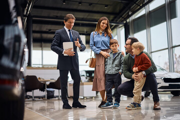 Happy family talking to salesman at car dealership.