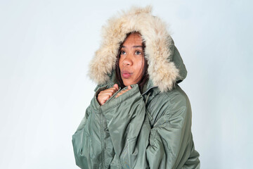 A cheerful Southeast Asian woman in a warm olive green winter coat with fur hood smiling over white background. © Ryan