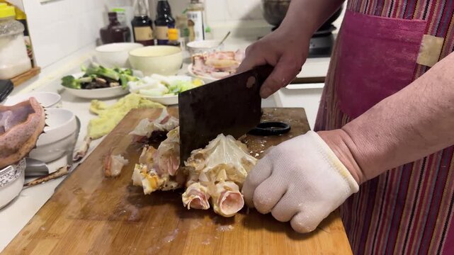 Preparing a live Shanghai hairy crab at home, with a cook cutting the crab using a large cleaver on a wooden cutting board to remove the meat from the hard shell before steaming in a kitchen setting.