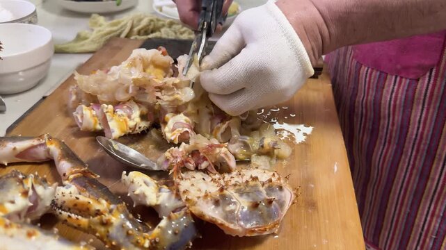 Preparing a live Shanghai hairy crab at home, with a cook cutting the crab using a large cleaver on a wooden cutting board to remove the meat from the hard shell before steaming in a kitchen setting.