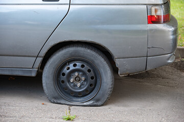Old gray car with a flat, deflated rear tire on asphalt, needing repair