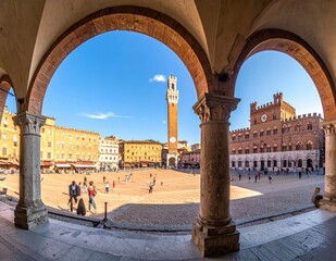 Naklejka premium Piazza del Campo in Siena, Italy, with Torre del Mangia and Palazzo Pubblico, viewed through historic arches.