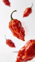 Several bright red ghost peppers falling and suspended in mid-air against a white background