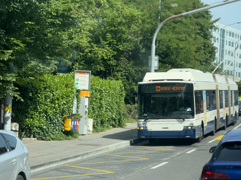 Geneva, switzerland - June 13 2025: A trolley bus on the road in Geneve Switzerland heads towards the Geneve Aeroport. The bus passes a bus stop with a trash can.