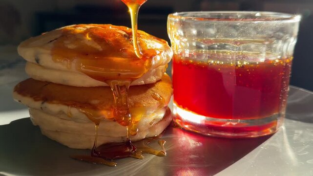 A close-up of golden honey  being poured over a stack of fluffy pancakes. This appetizing breakfast scene with honey dripping is perfect for food, cooking, and dessert content.