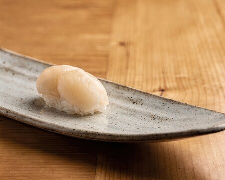 Fresh scallop sushi ingredient known as hotate placed on ceramic plate with natural light on wooden table, delicate Japanese seafood used in sushi and sashimi presented in minimal food still life