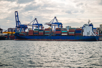 Fototapeta premium Cargo vessel docked at vladivostok port, stacked multicolored containers blocking cloudy maritime skyline